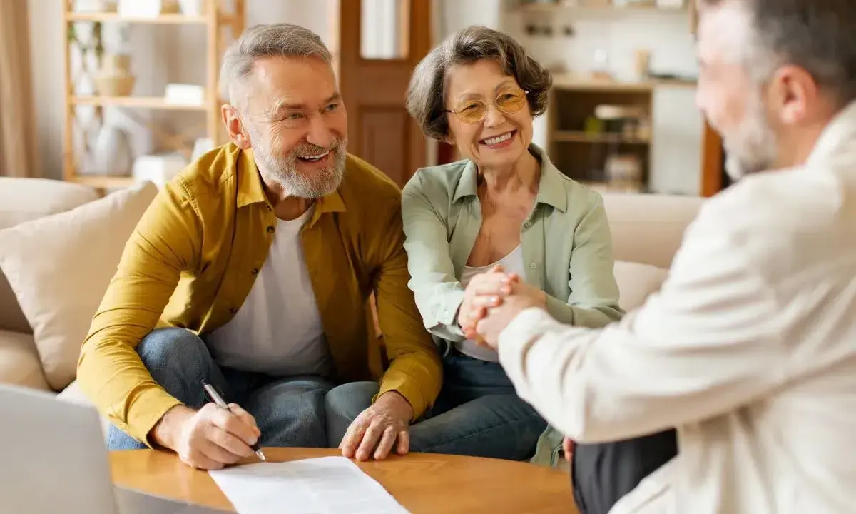 Couple âgé souriant discutant avec un conseiller, signature d'un prêt relais senior.
