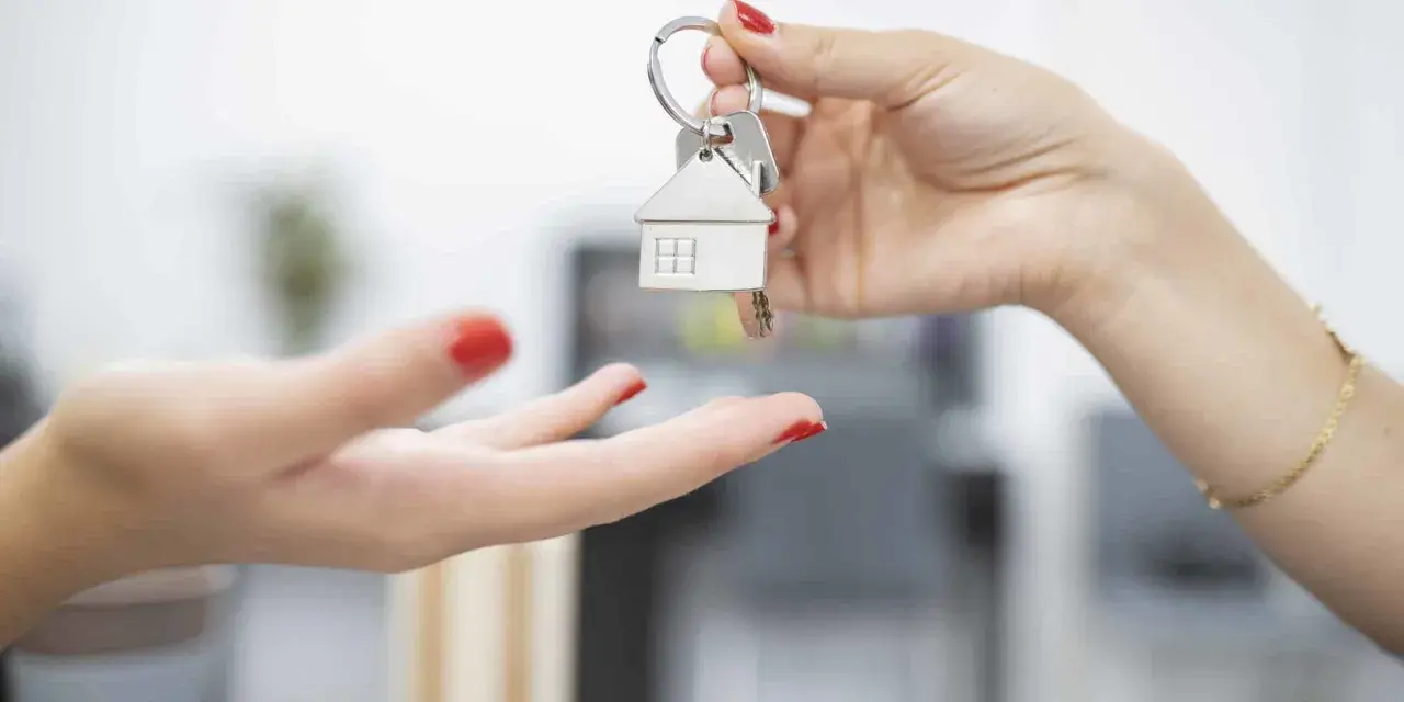 Une main tend des clés avec un pendentif maison. Le locataire reçoit les clés, prêt à emménager et à gérer ses impôts locaux.