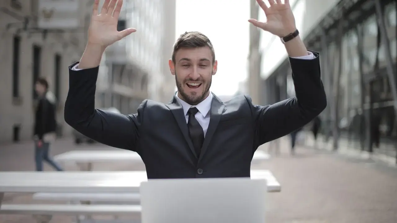 Homme en costume, bras levés, devant un ordinateur. Il semble avoir trouvé quel salaire pour emprunter 400 000 euros.