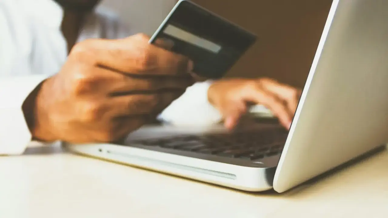 Homme utilisant une carte bancaire sur un ordinateur portable pour configurer un virement automatique de loyer avec son RIB.