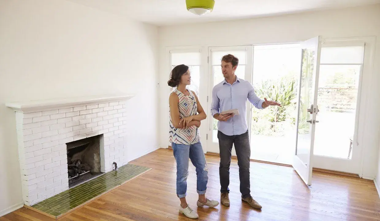 Un agent immobilier présente un appartement ou une maison à une cliente potentielle. La pièce est lumineuse, avec une cheminée en briques blanches et un sol en bois.