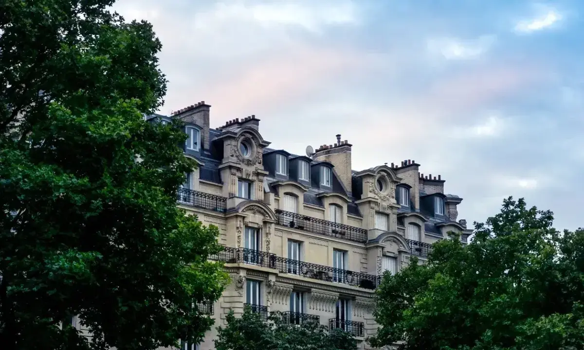 Immeuble haussmannien avec balcons en fer forgé, idéal pour une vente immeuble à rénover. Verdure luxuriante encadrant la façade.