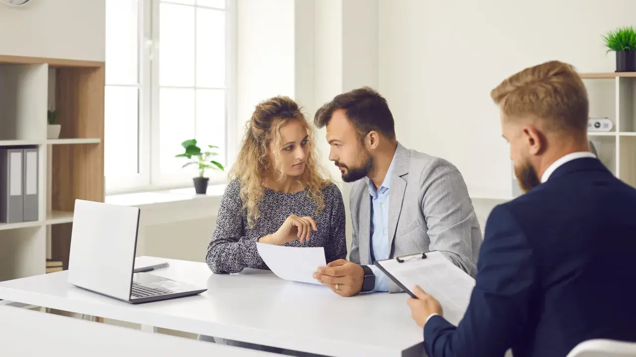 Un couple discute de documents avec un conseiller. Ils cherchent des solutions pour leur reste à vivre, une personne.