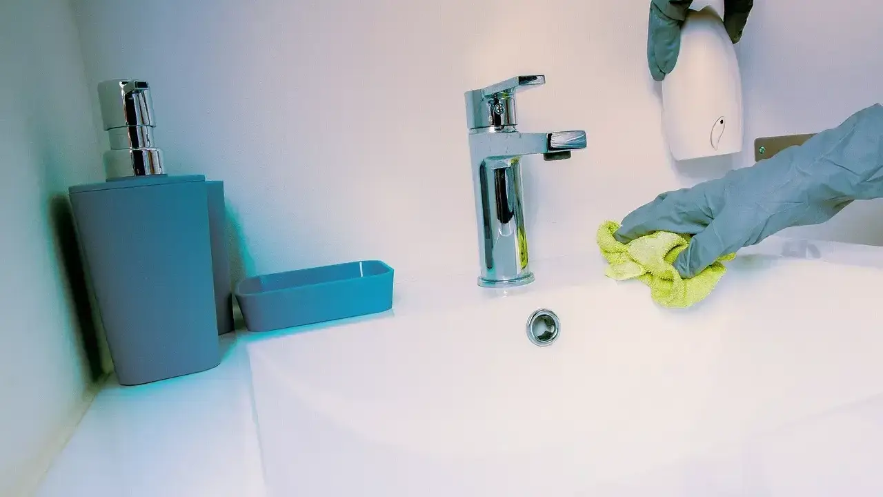 Mains de nettoyage avec un chiffon jaune, une retenue sur caution pour nettoyage. Un distributeur de savon et un robinet chromé sont visibles.