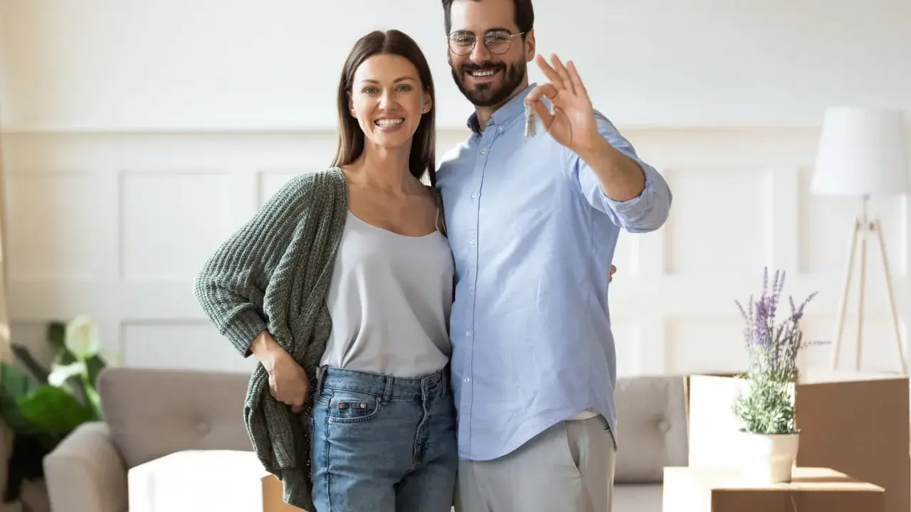 Couple heureux tenant les clés de leur nouvelle maison. L'homme fait le signe OK, symbolisant la réussite de leur projet immobilier, sans annulation offre d'achat par l'acheteur.
