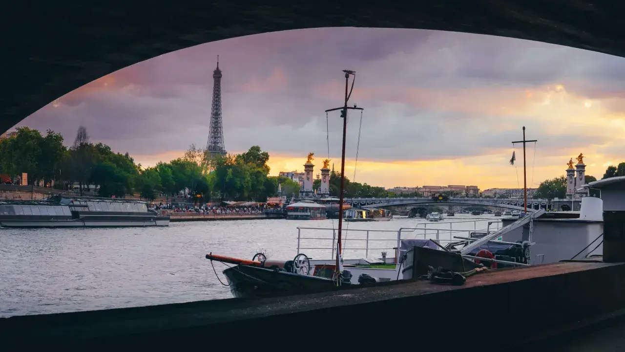 Vue de Paris au coucher du soleil, avec la Tour Eiffel en arrière-plan. Une péniche est amarrée, offrant un aperçu de la vie sur l'eau.