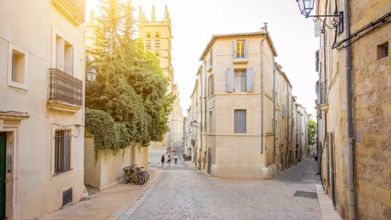 Ruelles pavées et bâtiments ocres, un aperçu des meilleurs quartiers de Montpellier. Des vélos attendent, des passants flânent sous le soleil.