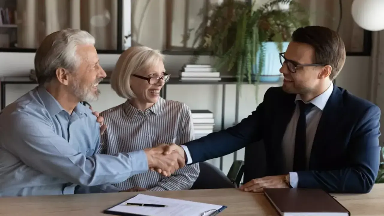 Un couple âgé serre la main d'un homme en costume. Ils sont co-emprunteurs mais pas propriétaires, un accord financier est signé.