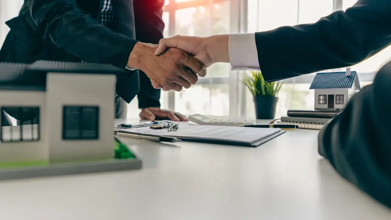 Poignée de main entre deux hommes d'affaires, symbolisant la réussite de la vente de son appartement. Maquettes de maisons sur la table.