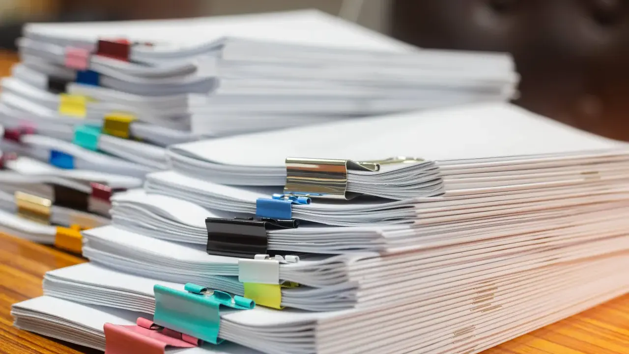 Piles de documents, certains reliés par des pinces colorées, prêts pour le service de la publicité foncière.
