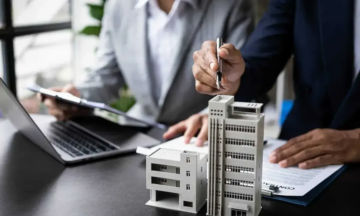 Deux personnes discutent de modèles de bâtiments et de documents, possiblement pour un projet immobilier ou un régime fiscal immobilier.