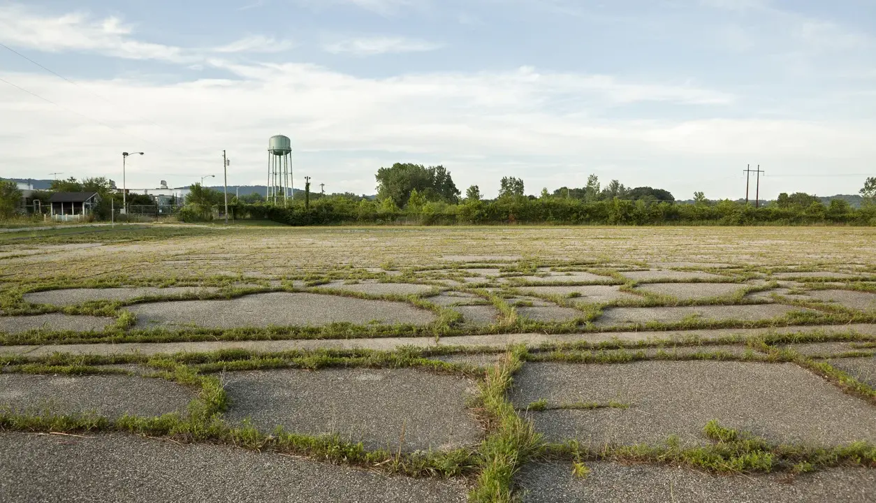 Vaste terrain vague avec des dalles de béton craquelées envahies par l'herbe. Idéal pour réfléchir à ce que peut on faire sur un terrain non constructible.