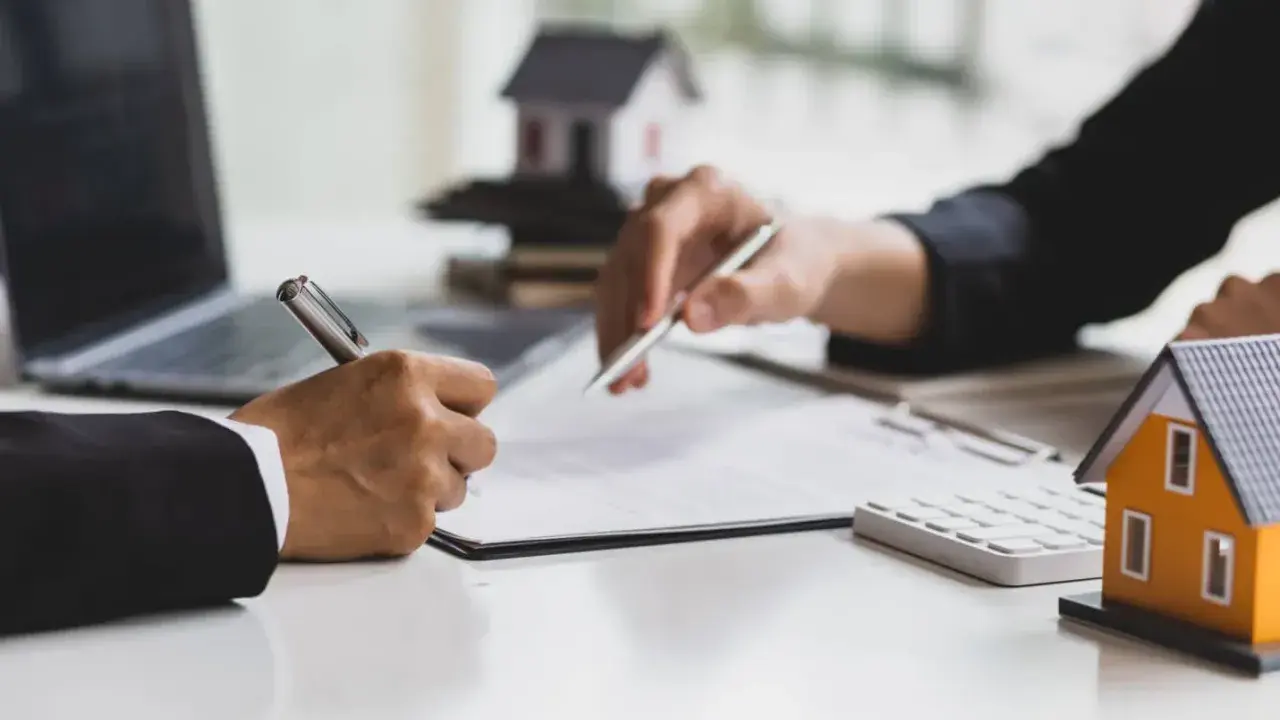 Signature d'un accord pour la résiliation d'un mandat exclusif après 3 mois. Des maisons miniatures et un ordinateur sont visibles.