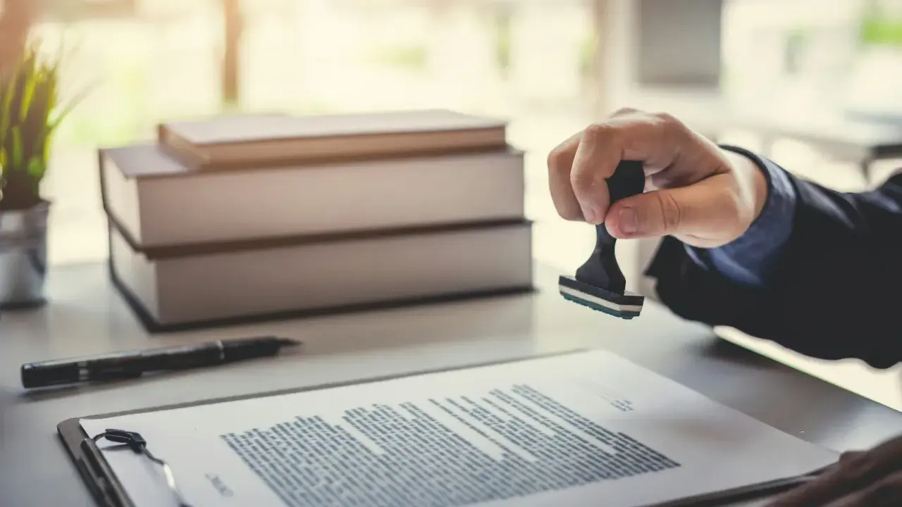 Main d'une personne apposant un tampon sur un document, scellant ainsi un titre de propriété.