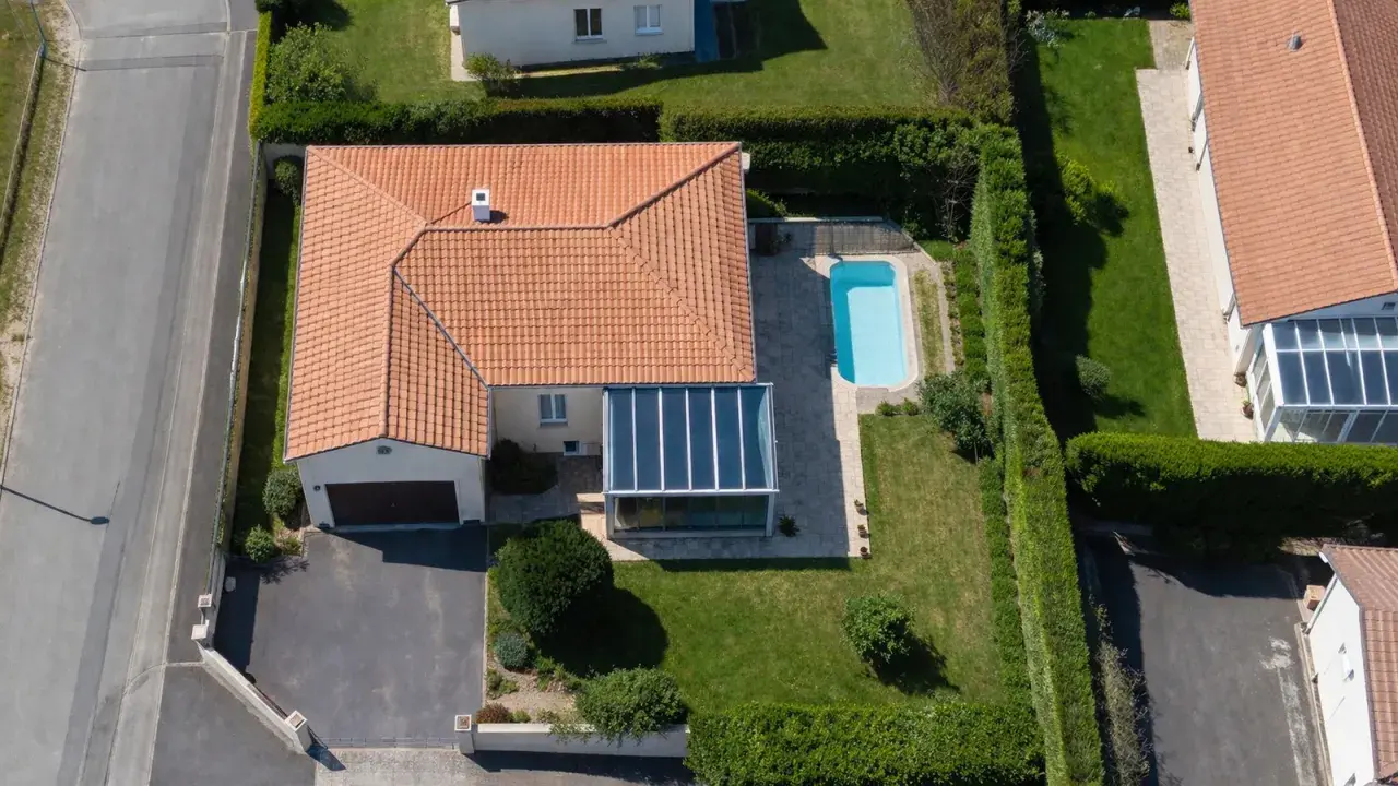 Vue aérienne d'une maison avec piscine et véranda. Une dépendance maison impôts, un garage et une allée complètent le paysage.