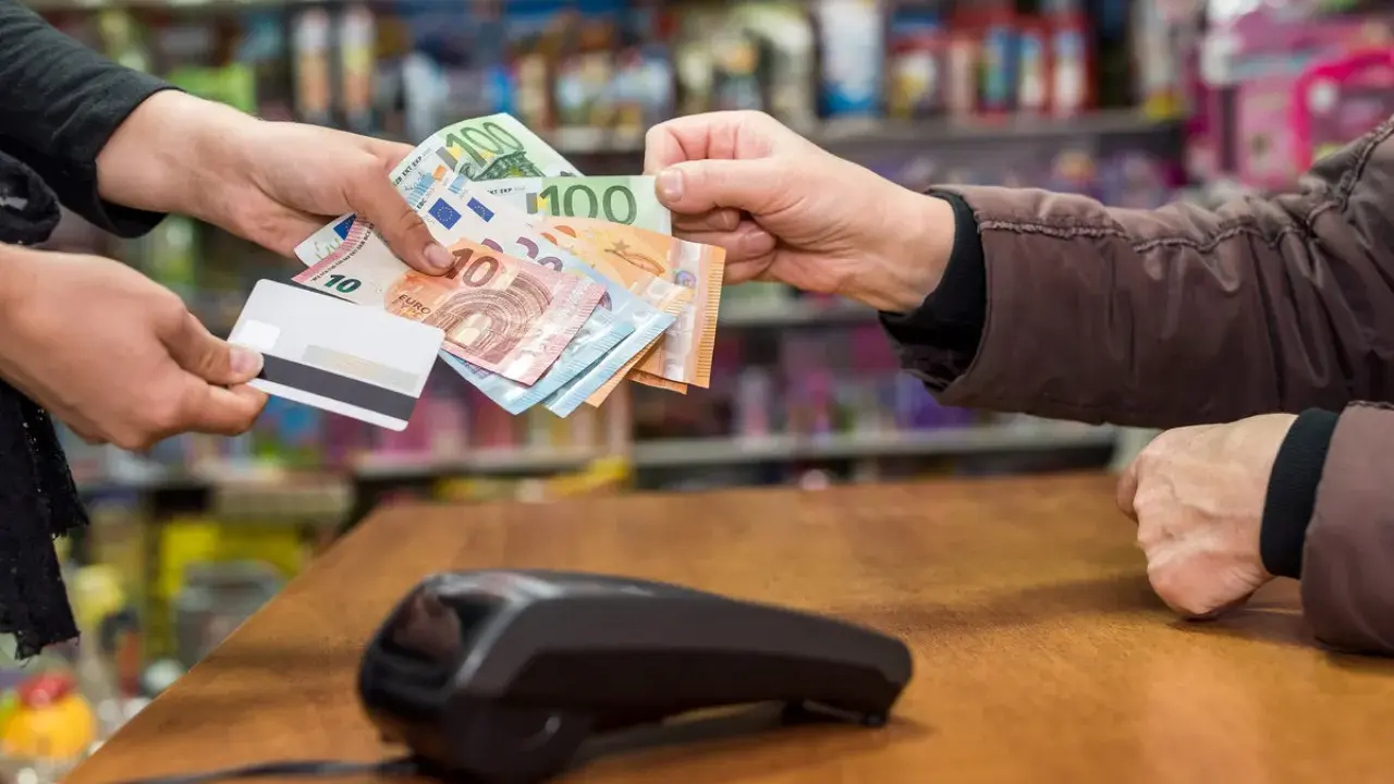 Une main tend des billets en euros et une carte bancaire. La question est : peut-on payer un artisan en liquide ?
