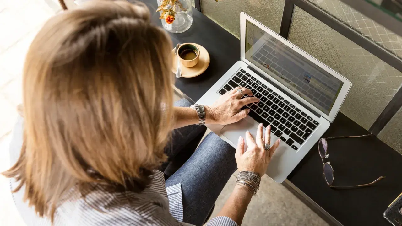 Femme tapant sur un ordinateur portable, une tasse de café à côté. Elle rédige peut-être une lettre recommandation locataire.