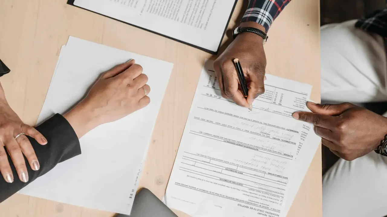 Des mains signent un compromis de vente sur un bureau en bois, entourées de documents.