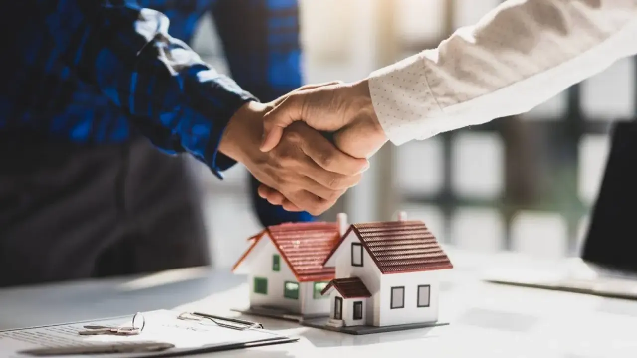 Poignée de main sur des maquettes de maisons, symbolisant un accord. Le compromis de vente délai dépassé par le vendeur est une préoccupation.