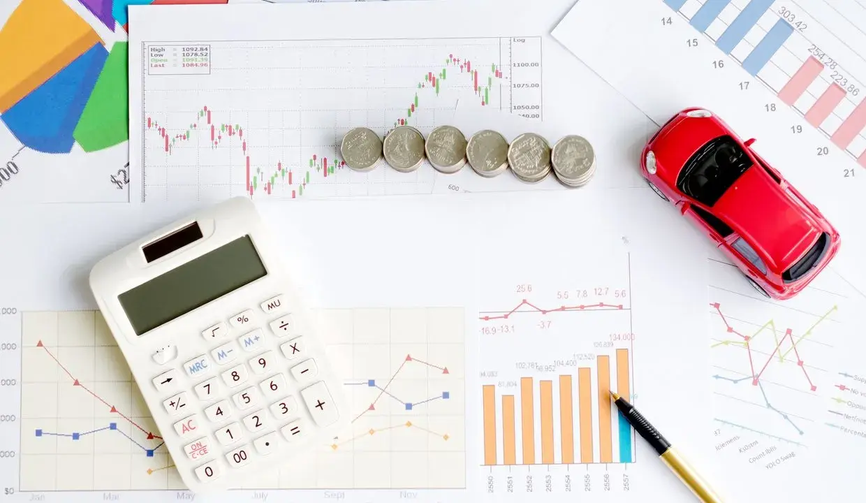 Calculatrice, pièces et voiture rouge sur des graphiques financiers. Idéal pour illustrer les frais de remboursement anticipé prêt immobilier.