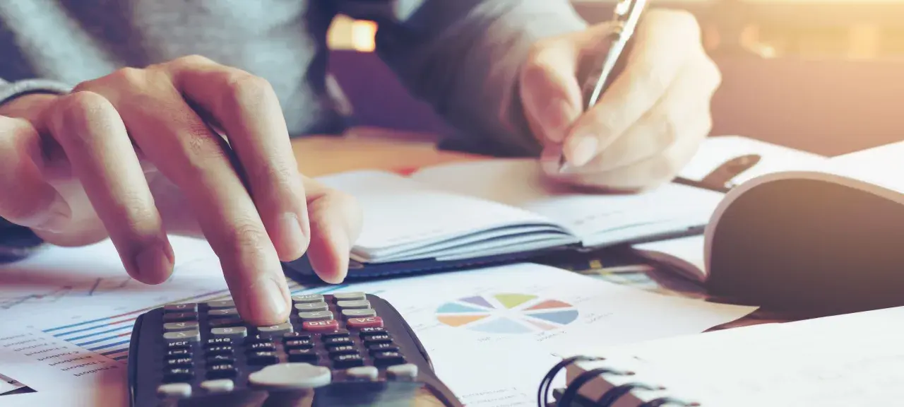 Calculatrice et stylo en main, une personne travaille sur un tableau d'amortissement d'un bien immobilier, entourée de graphiques.