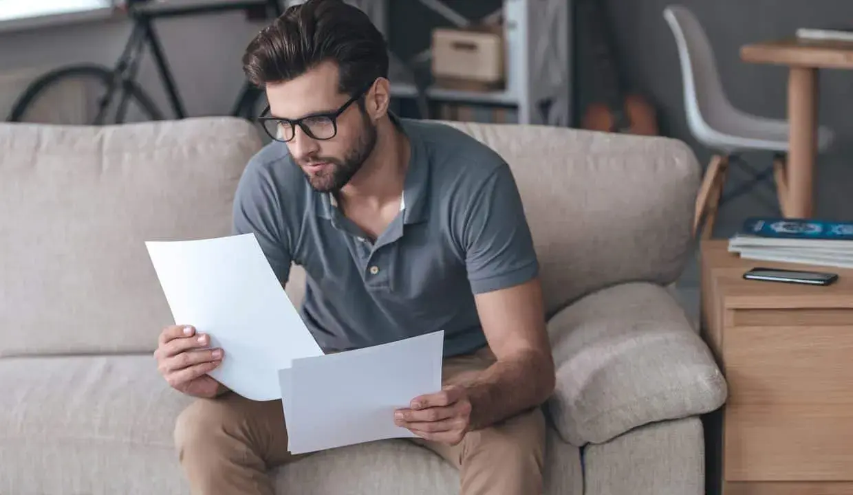 Homme concentré sur des documents, peut-être pour un crédit immobilier interimaire, assis sur un canapé.