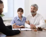Un couple signe des documents, possiblement un justificatif de propriété, avec un avocat.