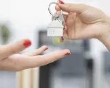 Une main tend des clés avec un pendentif maison. Le locataire reçoit les clés, prêt à emménager et à gérer ses impôts locaux.