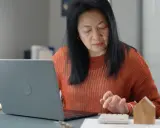 Femme calculant des frais de location avec un ordinateur portable et une calculatrice.