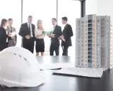Maquette d'immeuble, plans et casque blanc sur une table. Des professionnels discutent, peut-être des travaux sur parties communes sans autorisation.