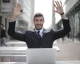 Homme en costume, bras levés, devant un ordinateur. Il semble avoir trouvé quel salaire pour emprunter 400 000 euros.