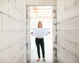 Femme souriante tenant un plan dans un chantier. Un acompte encaissé pour des travaux non réalisés, mais l'espoir est là.