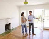 Un agent immobilier présente un appartement ou une maison à une cliente potentielle. La pièce est lumineuse, avec une cheminée en briques blanches et un sol en bois.