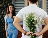 Un homme cache un bouquet de fleurs derrière son dos, prêt à surprendre sa compagne. Un couple non marié dans un lieu extérieur.