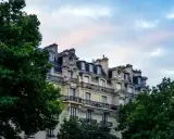 Immeuble haussmannien avec balcons en fer forgé, idéal pour une vente immeuble à rénover. Verdure luxuriante encadrant la façade.