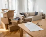 Clés et contrat de location sur une table en bois, cartons de déménagement empilés. Un nouveau départ dans une zone tendue.