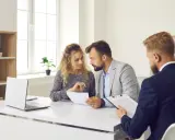 Un couple discute de documents avec un conseiller. Ils cherchent des solutions pour leur reste à vivre, une personne.