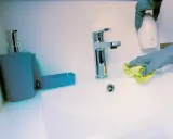 Mains de nettoyage avec un chiffon jaune, une retenue sur caution pour nettoyage. Un distributeur de savon et un robinet chromé sont visibles.