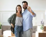 Couple heureux tenant les clés de leur nouvelle maison. L'homme fait le signe OK, symbolisant la réussite de leur projet immobilier, sans annulation offre d'achat par l'acheteur.