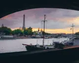 Vue de Paris au coucher du soleil, avec la Tour Eiffel en arrière-plan. Une péniche est amarrée, offrant un aperçu de la vie sur l'eau.