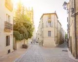 Ruelles pavées et bâtiments ocres, un aperçu des meilleurs quartiers de Montpellier. Des vélos attendent, des passants flânent sous le soleil.