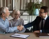 Un couple âgé serre la main d'un homme en costume. Ils sont co-emprunteurs mais pas propriétaires, un accord financier est signé.