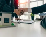 Poignée de main entre deux hommes d'affaires, symbolisant la réussite de la vente de son appartement. Maquettes de maisons sur la table.