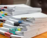Piles de documents, certains reliés par des pinces colorées, prêts pour le service de la publicité foncière.