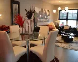 Table à manger moderne avec chaises blanches, parfaite pour une lmnp residence secondaire. Salon cosy avec canapés en cuir et tapis graphique.