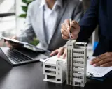 Deux personnes discutent de modèles de bâtiments et de documents, possiblement pour un projet immobilier ou un régime fiscal immobilier.
