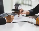 Signature d'un accord pour la résiliation d'un mandat exclusif après 3 mois. Des maisons miniatures et un ordinateur sont visibles.
