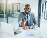 Un homme d'affaires souriant tend la main pour une poignée de main, mais le vendeur ne veut plus vendre. Il est assis à un bureau avec un ordinateur portable et une tasse de café.