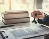 Main d'une personne apposant un tampon sur un document, scellant ainsi un titre de propriété.