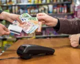 Une main tend des billets en euros et une carte bancaire. La question est : peut-on payer un artisan en liquide ?